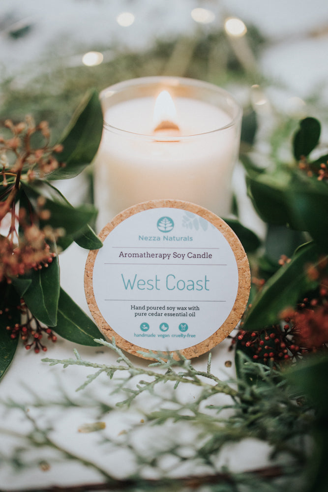 Nezza Naturals Aromatherapy soy candle in  'West Coast' surrounded by greenery and flowers.